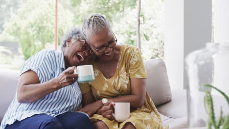 Happy-senior-african-american-female-friends-having-coffee-and-laughing-in-living-room,-slow-motion