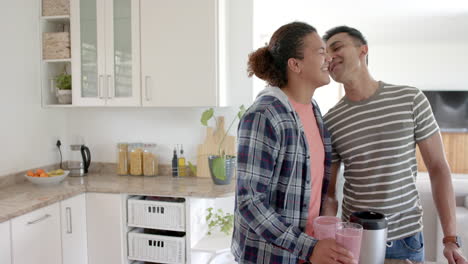 Happy-diverse-gay-male-couple-making-fruit-smoothie-and-kissing-in-kitchen,-copy-space,-slow-motion