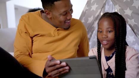 Glücklicher-Afroamerikanischer-Vater-Mit-Tochter,-Die-Ein-Tablet-Im-Tipi-Benutzt,-Zeitlupe