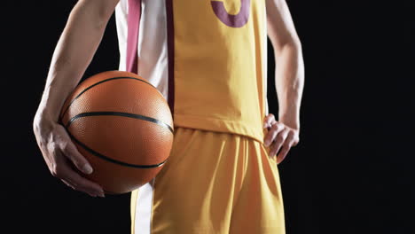 Weibliche-Basketballspielerin-In-Einer-Basketballuniform-Hält-Einen-Ball-Auf-Schwarzem-Hintergrund
