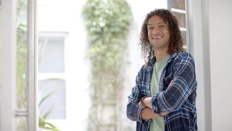 Portrait-of-biracial-man-with-long-curly-hair-smiling-in-doorway-at-home,-copy-space,-slow-motion