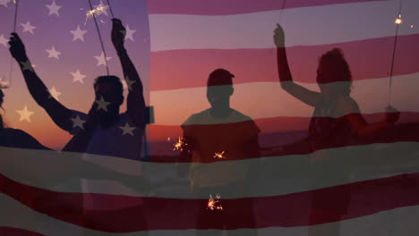 Animation-Der-Amerikanischen-Flagge-über-Fröhlichen,-Unterschiedlichen-Freunden,-Die-Mit-Wunderkerzen-Am-Strand-Bei-Sonnenuntergang-Tanzen