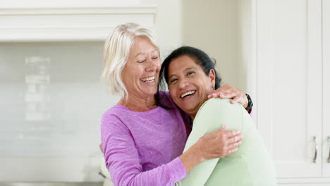 Two-happy-diverse-senior-women-embracing-and-smiling-in-sunny-kitchen,-slow-motion