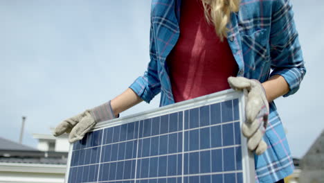 Portrait-of-happy-cauasian-woman-with-gloves-holding-solar-panel-in-garden,-slow-motion