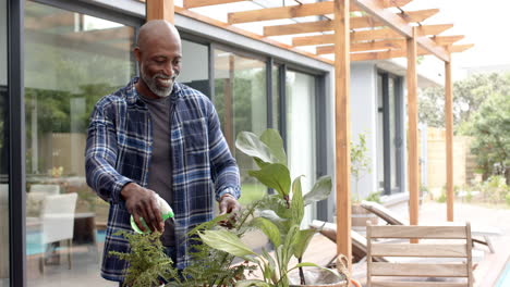 Glücklicher-Reifer-Afroamerikanischer-Mann,-Der-Pflanzen-Auf-Der-Gartenterrasse-Gießt,-Zeitlupe