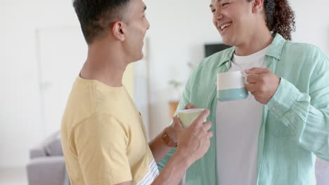 Happy-diverse-gay-male-couple-having-coffee,-standing-and-talking-at-home,-copy-space,-slow-motion
