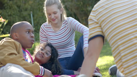 Happy-diverse-group-of-teenage-friends-sitting-on-grass-and-talking-in-sunny-park,-slow-motion