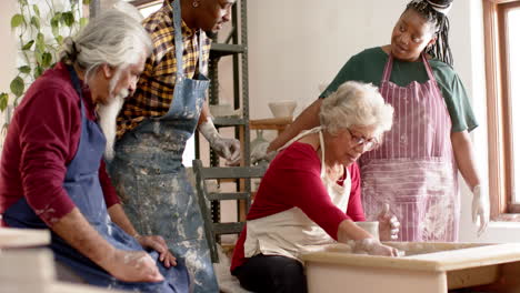 Happy-biracial-female-potter-with-others,-using-potter's-wheel-in-pottery-studio,-slow-motion