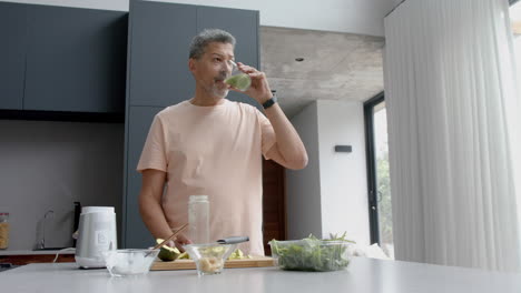 Happy-senior-biracial-man-drinking-healthy-smoothie-in-kitchen-at-home,-copy-space,-slow-motion