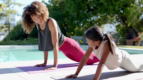 Happy-biracial-mother-and-daughter-practicing-yoga-pose-in-sunny-garden,-slow-motion