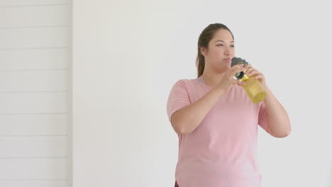 Happy-plus-size-biracial-woman-drinking-from-water-bottle-after-exercising,-copy-space,-slow-motion