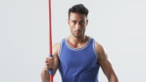 Young-biracial-athlete-man-holds-a-javelin-in-a-clean-indoor-setting-on-a-white-background