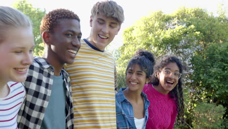Happy-diverse-group-of-teenage-friends-embracing-in-sunny-park,-slow-motion