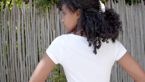 Rear-view-of-biracial-woman-with-long-hair-in-white-t-shirt-with-hands-on-hips-outdoors,-slow-motion