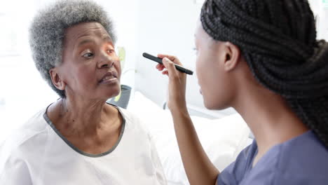 Afroamerikanische-Ärztin-Testet-Die-Augen-Einer-älteren-Patientin-Im-Krankenhauszimmer,-Zeitlupe