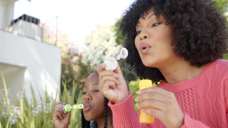 Happy-african-american-mother-with-daughter-blowing-bubbles-in-garden-at-home,-slow-motion