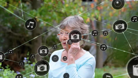 Animation-of-network-of-connected-icons-in-circles-over-senior-caucasian-woman-using-smartphone