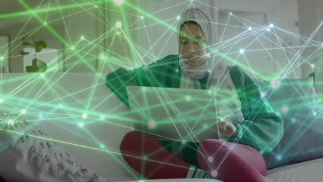 Animación-De-La-Red-De-Conexiones-Sobre-Una-Mujer-Birracial-Con-Hijab-Usando-Una-Computadora