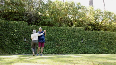 Happy-biracial-senior-couple-dancing-in-sunny-garden