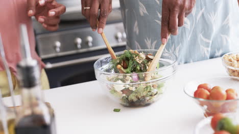 Midsection-of-senior-african-american-female-friends-preparing-salad-in-kitchen,-slow-motion