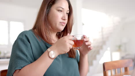 Focused-plus-size-biracial-woman-drinking-tea-while-using-laptop,-working-from-home,-slow-motion