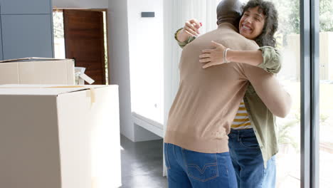 Happy-biracial-couple-embracing-with-cartons-at-new-house,-slow-motion
