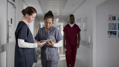Diverse-female-doctors-discussing-work,-using-tablet-in-corridor-at-hospital,-slow-motion