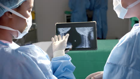 Diverse-female-surgeons-looking-at-x-ray-scans-on-tablet-in-operating-theatre,-slow-motion