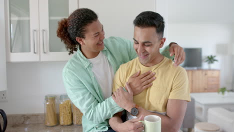 Happy-diverse-gay-male-couple-having-coffee-and-embracing-in-sunny-kitchen,-slow-motion