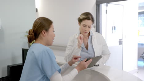 Focused-diverse-female-doctors-using-tablet-and-discussing-over-hospital-reception-desk,-slow-motion