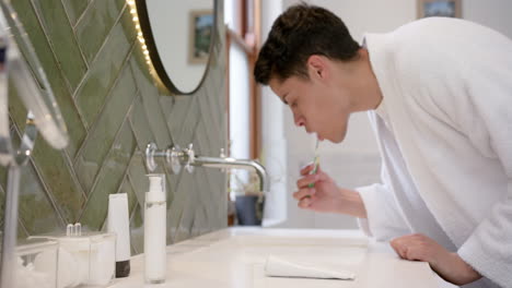 Biracial-man-brushing-teeth-in-morning-in-bathroom,-copy-space,-slow-motion