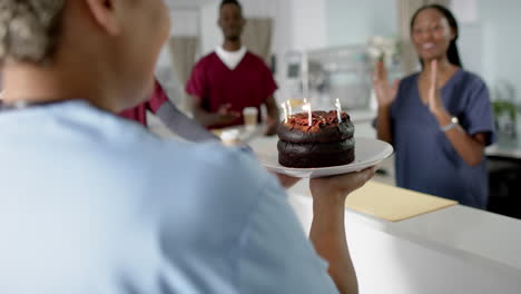 Diverse-male-and-female-doctors-celebrating-birthday-at-reception-desk-at-hospital,-slow-motion