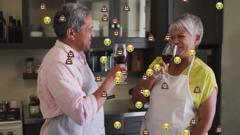 Animation-Von-Emoji-Symbolen-über-Einem-älteren-Gemischtrassigen-Paar,-Das-In-Der-Küche-Wein-Trinkt