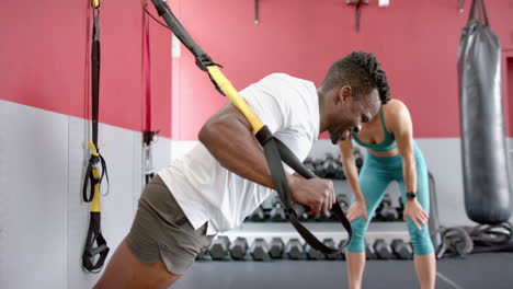 Fitter-Afroamerikaner-Trainiert-Eine-Junge-Kaukasische-Frau-Im-Fitnessstudio