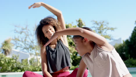 Happy-biracial-mother-and-daughter-practicing-yoga-stretching-in-sunny-garden,-slow-motion