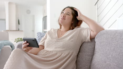 Happy-plus-size-biracial-woman-having-smartphone-video-call-in-sunny-living-room,-slow-motion