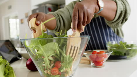 Afroamerikanische-Seniorin-Mischt-Salat-In-Sonniger-Küche,-Zeitlupe