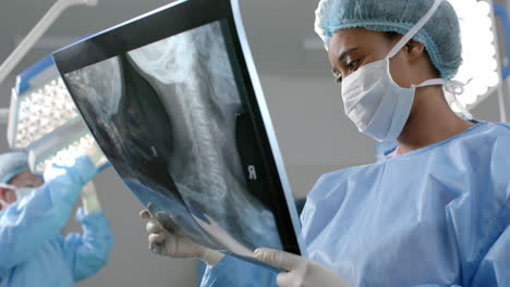 African-american-female-surgeon-looking-at-x-ray-scans-in-operating-theatre,-slow-motion