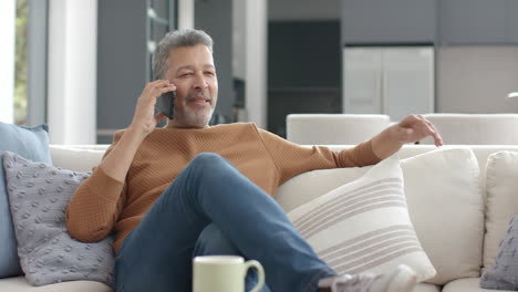 Glücklicher-älterer-Mann-Mit-Gemischter-Abstammung,-Der-Auf-Dem-Smartphone-Auf-Der-Couch-Im-Wohnzimmer-Spricht,-Platz-Zum-Kopieren,-Zeitlupe