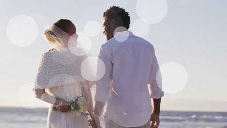 Animation-Von-Lichtpunkten-über-Einem-Afroamerikanischen-Paar,-Das-Am-Strand-Heiratet