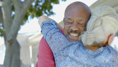 Happy-senior-biracial-couple-embracing-in-sunny-garden-at-home,-slow-motion