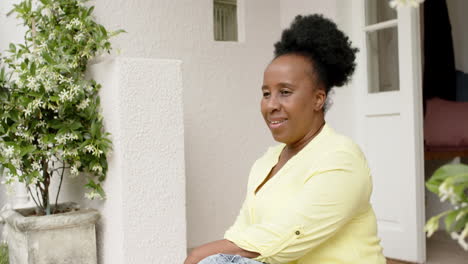 Glückliche-Afroamerikanische-Seniorin,-Die-Vor-Dem-Haus-Sitzt-Und-Lächelt,-Zeitlupe