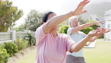 Two-focused-diverse-senior-women-practising-yoga-in-sunny-garden,-slow-motion,-copy-space