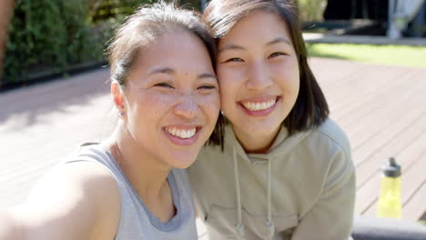 Glückliche-Asiatische-Freundinnen-Mit-Wasserflasche-Machen-Selfie-Und-Lachen-Auf-Der-Terrasse,-Zeitlupe