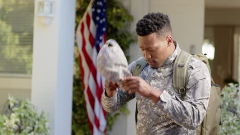 Serious-african-american-male-soldier-putting-cap-on-over-flag-of-usa-at-home,-slow-motion