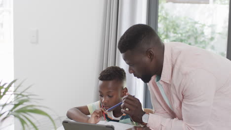 Afroamerikanischer-Vater-Hilft-Sohn-Zu-Hause-Mit-Einem-Tablet-Bei-Den-Hausaufgaben