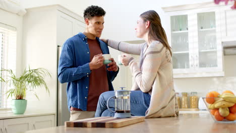 Happy-diverse-couple-talking-and-drinking-coffee-in-kitchen-at-home,-in-slow-motion