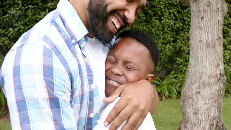 Glücklicher-Afroamerikanischer-Vater-Und-Sohn-Umarmen-Und-Lächeln-Im-Garten,-Zeitlupe