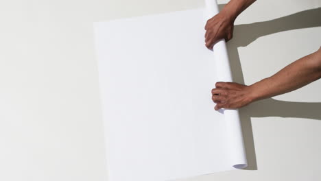 Video-of-hands-of-african-american-man-with-rolling-up-white-paper-on-white-background