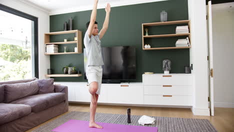 Fokussierter-Biracial-Mann,-Der-Yoga-Praktiziert-Und-Auf-Einem-Bein-Im-Wohnzimmer-Steht,-Kopierraum,-Zeitlupe